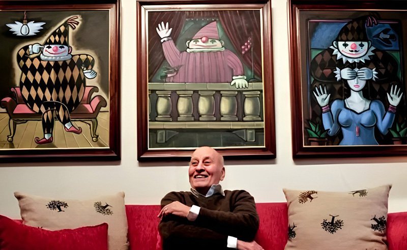 Helmi El-Touni seated beneath three of his harlequin paintings