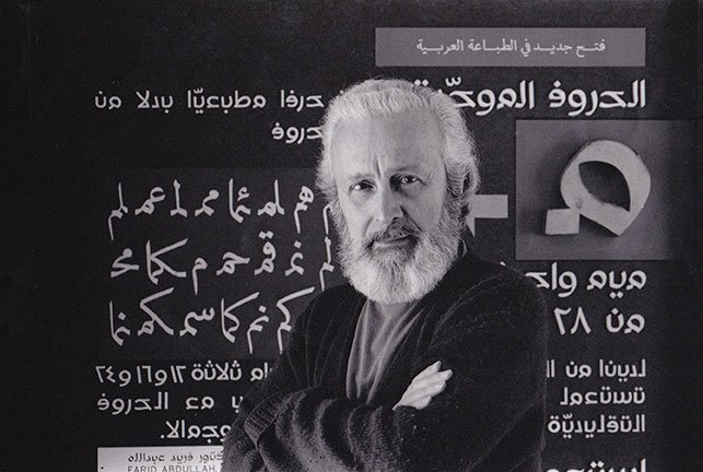 Nasri Khattar, bearded, standing in front of a Unified Arabic display